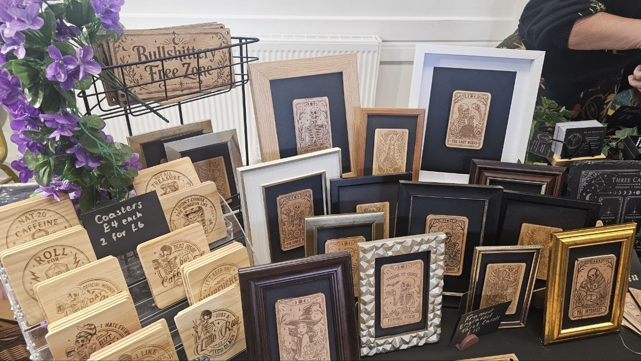 Framed engraved cards and wooden coasters displayed with foxglove-purple flowers
